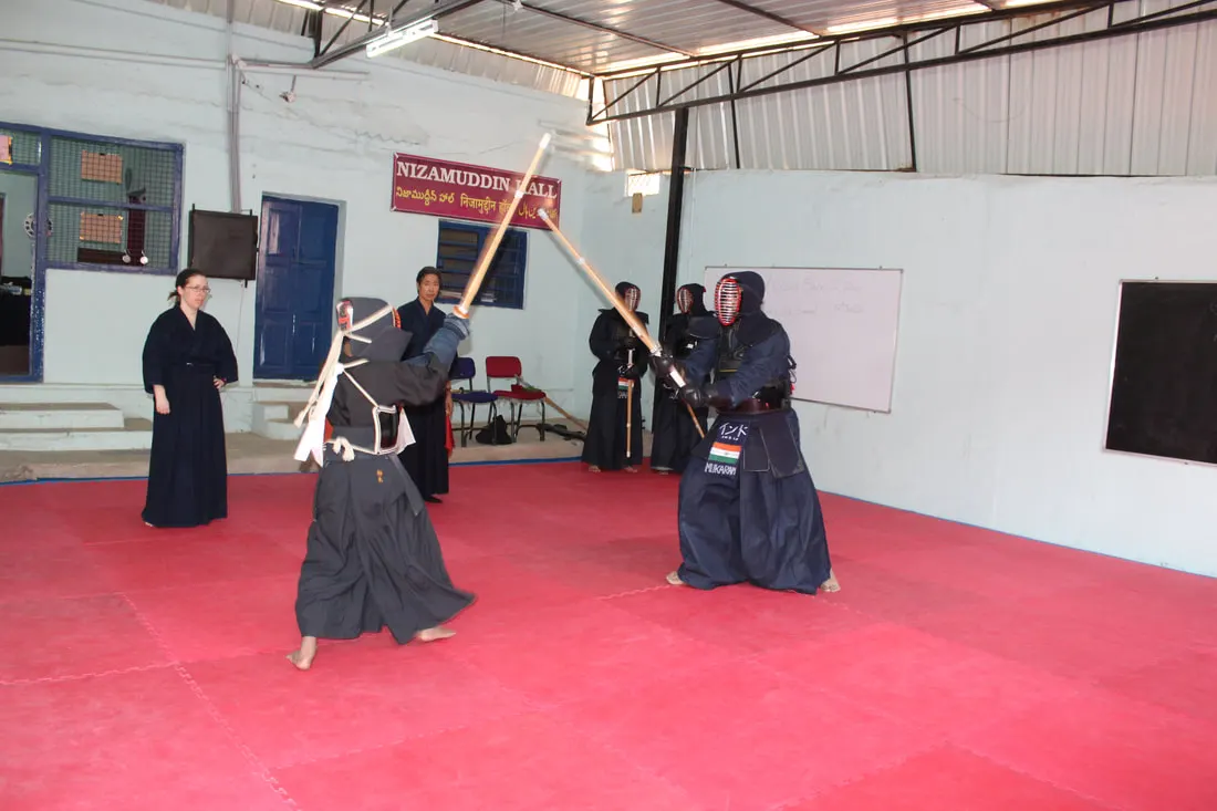 Two kendoka sparring in armour on red mats while others watch